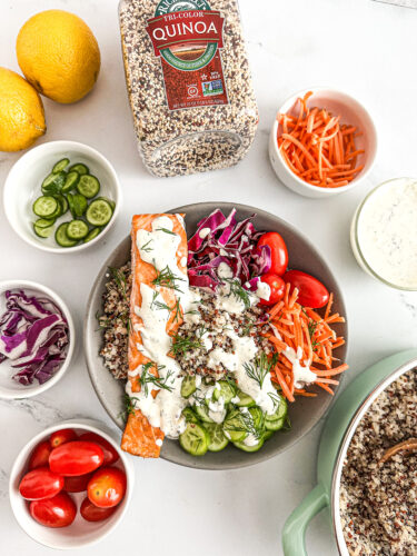 large bowl filled with fluffy quinoa spiced salmon carrots tomatoes cabbage cucumbers and lemon dill dressing 